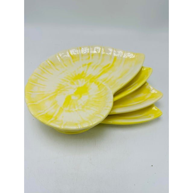 This is a set of four ceramic shell-shaped dishes with a bright yellow and white marbled glaze, designed to mimic the...