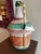 A richly colored vintage demijohn bottle wrapped in handwoven orange, green, and white vinyl, bringing texture,...