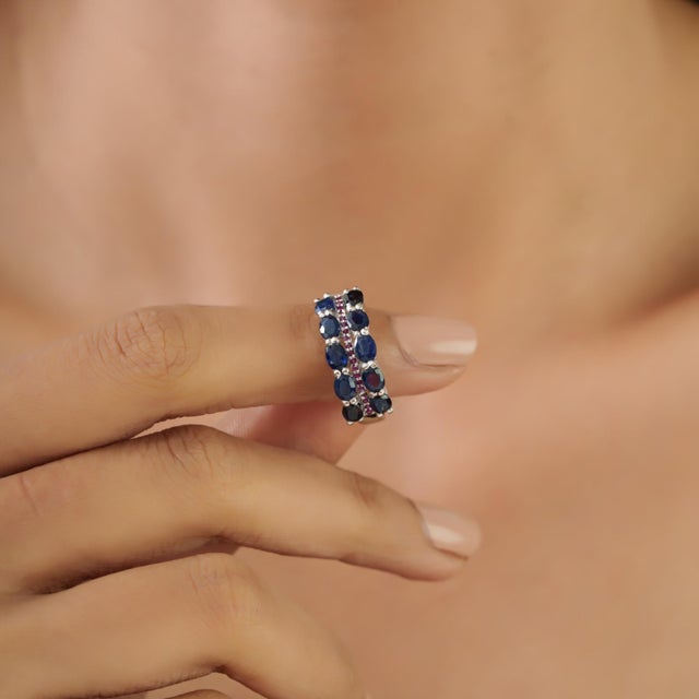 This elegant multi-row band ring features 2.29 carats of oval blue sapphires accented with vibrant rubies, handcrafted in...
