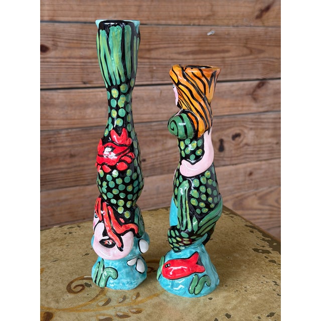 Playful pair of hand-painted ceramic mermaid candlestick holders featuring bold colors, sculptural detailing, and lots of...