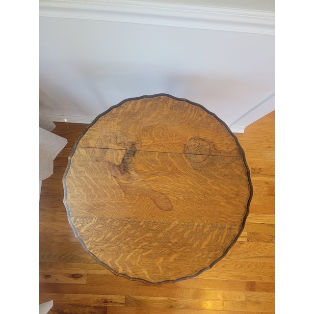 Antique round oak parlor or occasional table dating to the early 20th century. The table features a scalloped molded top...