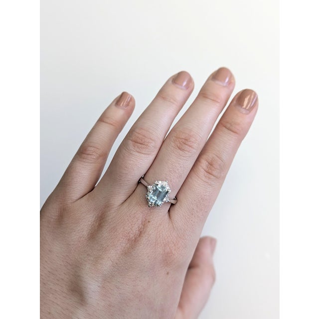 This pretty ring features a 1.5 carat emerald-cut aquamarine glowing with icy blue beauty, encircled by earth-mined...