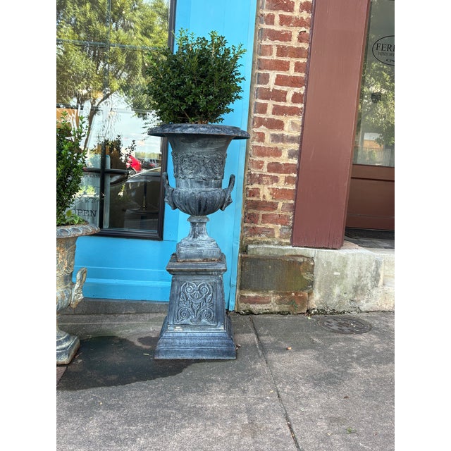A distinguished pair of cast iron urns mounted on stands, each 41 inches in height with a 19-inch top diameter. These...