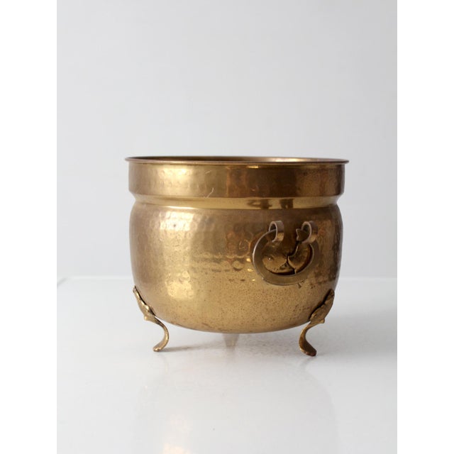 Antique Victorian brass jardiniere featuring a hammered brass body, ring handles, and decorative claw feet. The rounded...
