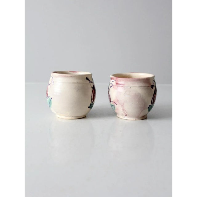 A pair of vintage studio pottery mugs, hand-crafted with a soft cream and pink glaze. Each mug features a hand-painted...