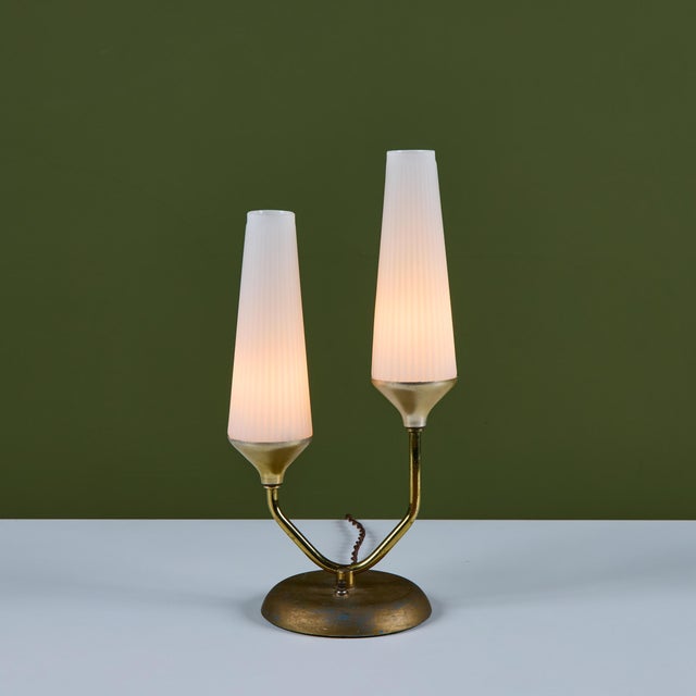 Brass table lamp features aged brass stems on a pedestal base with two fluted milk glass cone shades. The switch at the...