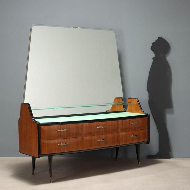 Dresser with mirror and glass shelf, exotic wood veneer, top with back-treated glass, brass details. This piece is...