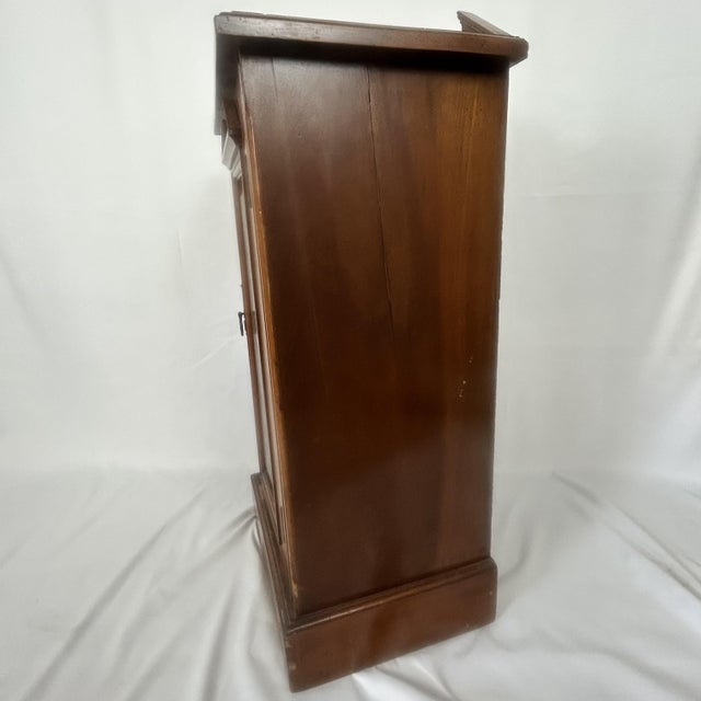 A charming antique late Victorian walnut bedside cabinet dating from circa 1890. It has a single carved paneled door with...