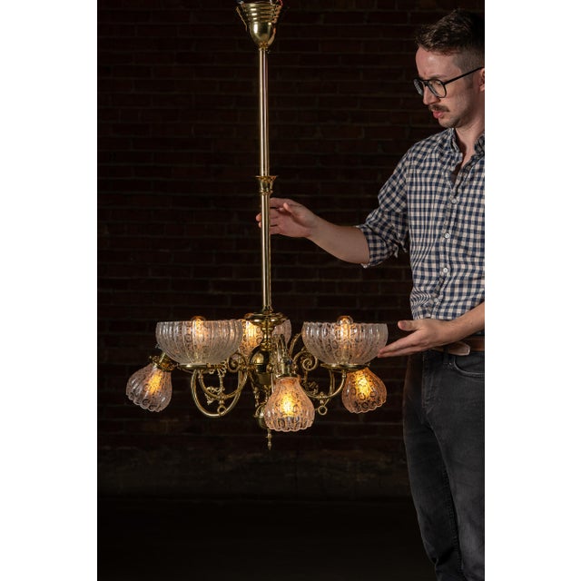 A bright brass chandelier with six elegantly curved arms, each fitted with a deeply ribbed etched glass shade. The design...