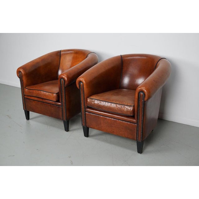 This pair of cognac-colored leather club chairs come from the Netherlands. They are upholstered with cognac-colored...