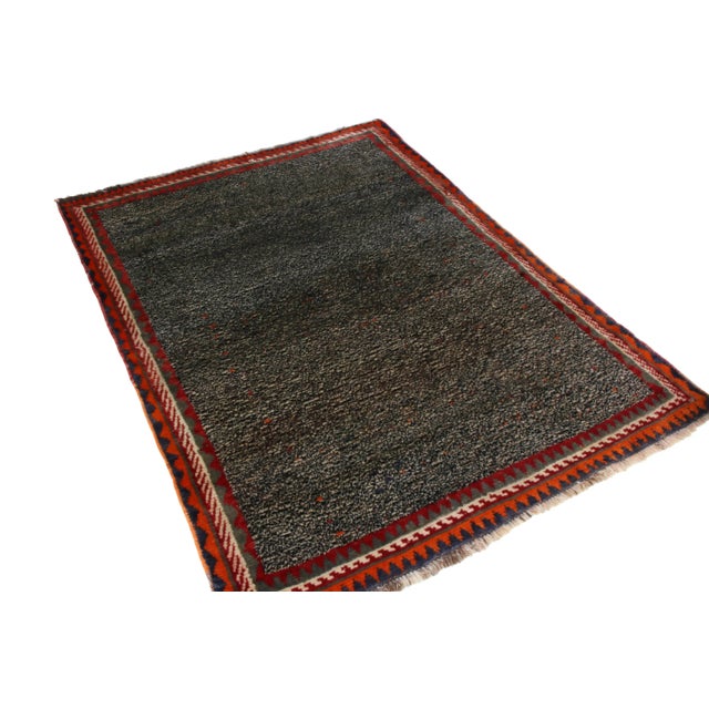 Made with hand-knotted wool originating between 1910-1920, this antique Gabbeh Persian rug enjoys the tactful...