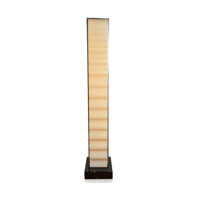 A wavy acrylic glass lampshade rests on a geometric base of black lacquered aluminum, its silhouette resembling a stylized...