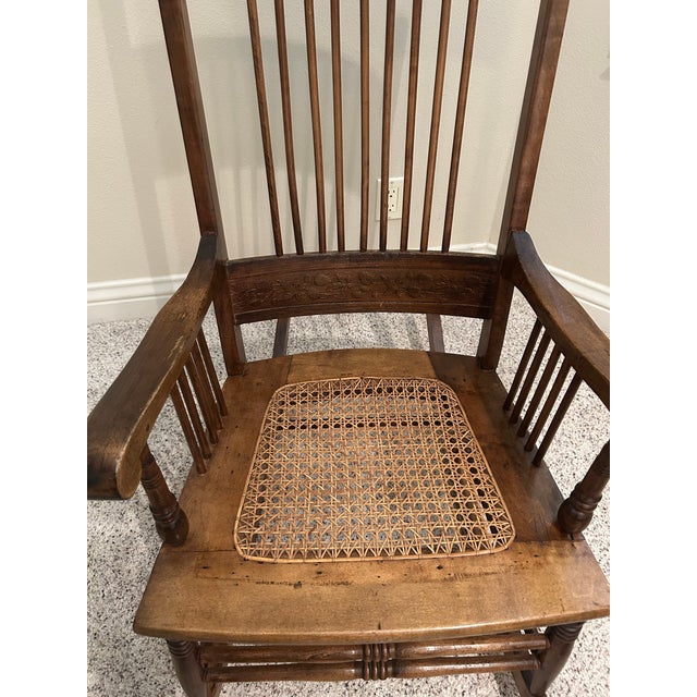 Beautiful vintage high-backed oak rocking chair featuring hand-carved floral details, a woven cane seat, and gracefully...