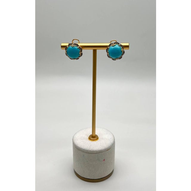 These striking earring features a vibrant turquoise cabochon, set within a detailed, scalloped bezel. The bezel is adorned...