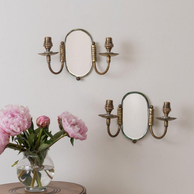 Beautiful pair of brass and mirror sconces from France, 1940s. Oval beveled mirror with two curved brass arms and ball...