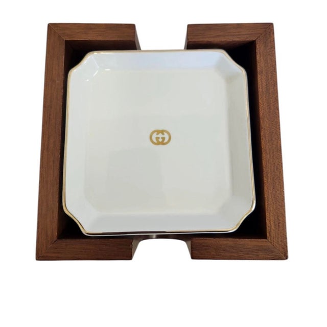 Gucci Ashtray or Coaster Set with Wooden Holder. 6 ceramic coasters with a Gucci holder. White porcelain with gilded edges...
