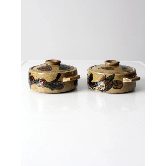A pair of vintage studio pottery covered serving dishes featuring hand-painted floral motifs and raised decorative...
