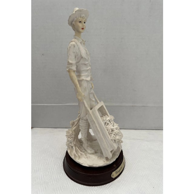 Blanc sur Blanc figurine that depicts a gentleman farmer holding a wheelbarrow full of grapes. He is wearing short...
