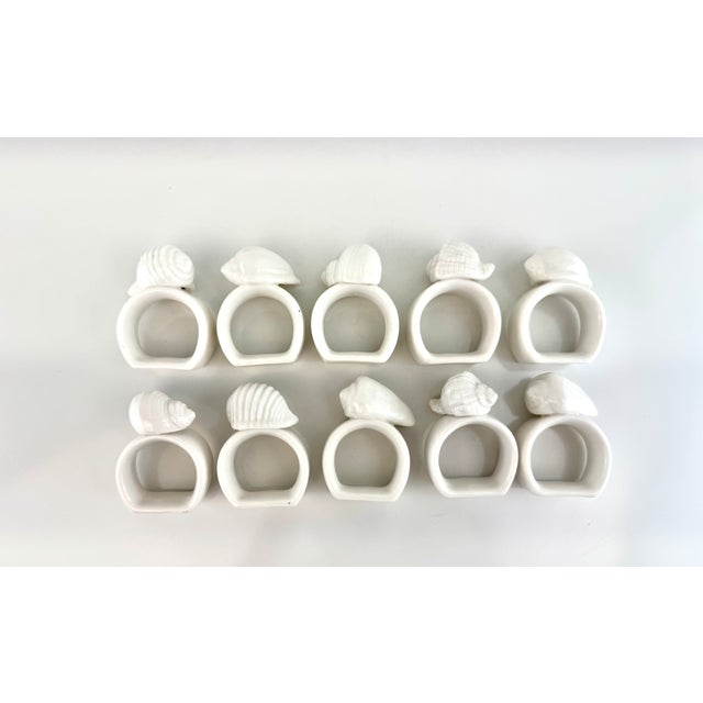 A charming set of ten white ceramic napkin rings, each topped with sculptural seashell forms in a variety of naturalistic...