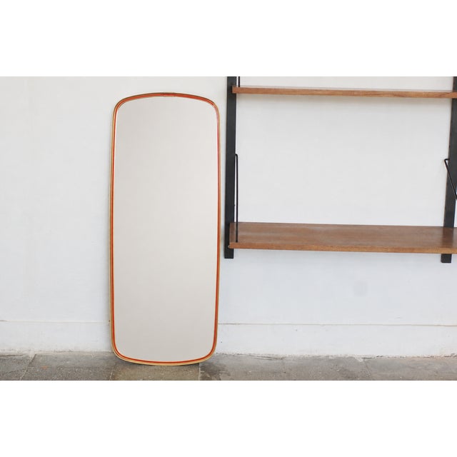 A slender vintage wall mirror with a distinctive, elongated shape and softly rounded corners. Its minimalist silhouette...