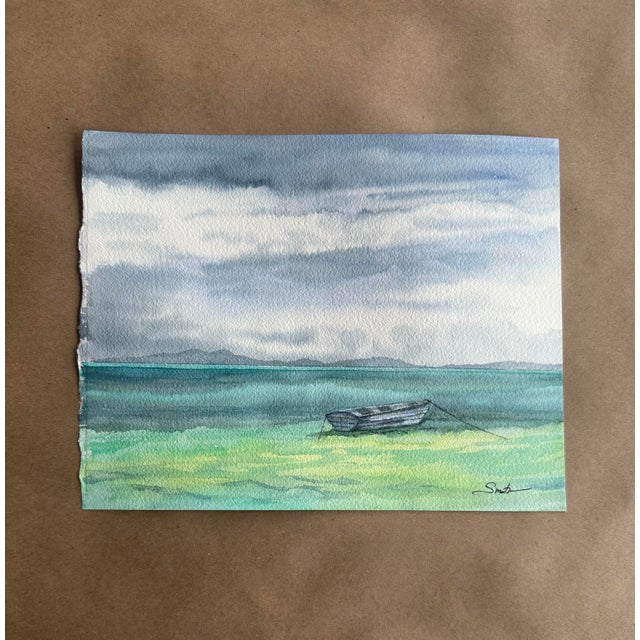 A serene original watercolor capturing a tranquil coastal scene, featuring a solitary drift boat resting along a soft...
