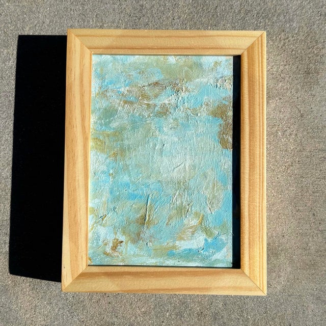 This textured abstract painting layers soft blues, pale aquas, and muted golds into a quietly luminous surface. Broad,...
