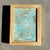 This textured abstract painting layers soft blues, pale aquas, and muted golds into a quietly luminous surface. Broad,...
