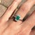 An emerald rests in a rich green at the centre of this solid 14K white gold ring, surrounded by twelve earth-mined...