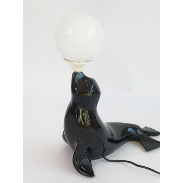 A stunning original regency vintage black glazed ceramic table lamp in the shape of a seal holding a white globe. Black...