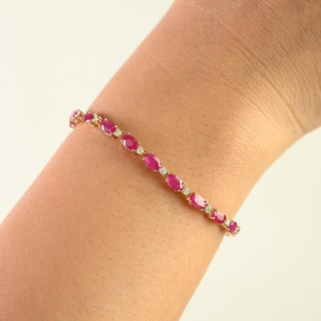 This elegant tennis bracelet features 25 oval cut natural rubies totaling 6.93 carats, set in rich 14k yellow gold. Each...