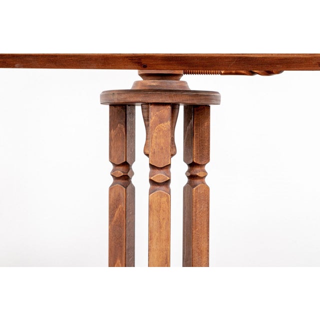A carved wooden music stand in a warm honey-brown finish with a natural wood grain, an open triple turned columnar frame,...