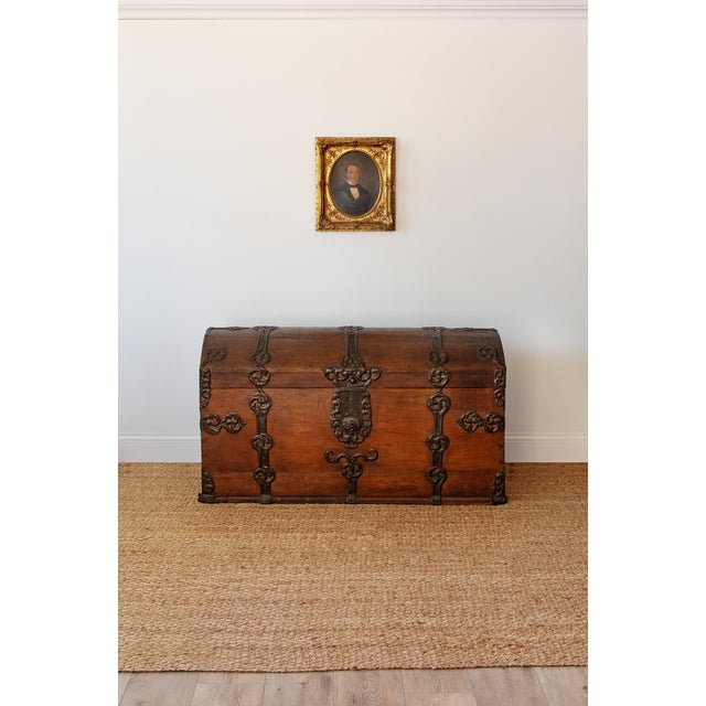 A commanding dome-top coffer in oak, bound front and lid with hand-wrought iron strapwork in scrolling foliate forms. The...