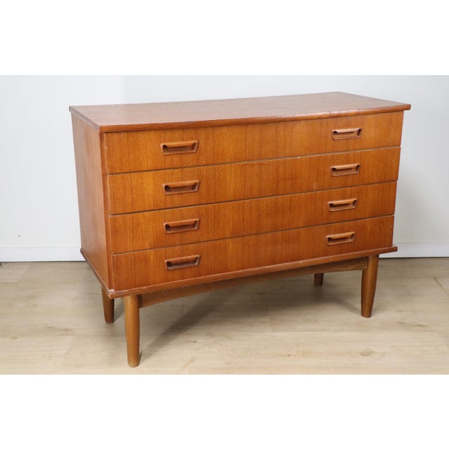 A 1960s Scandinavian chest of drawers in teak veneer, characterized by its clean lines and functional design. It rests on...