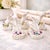 A charming set of vintage porcelain place card holders shaped like elegant sculpted hands, each accented with delicate...