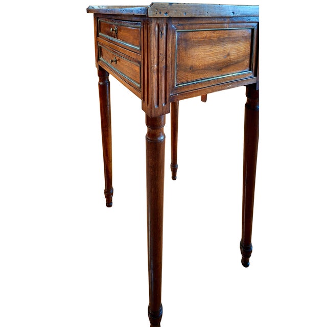 On offer is a French Louis XVI-style mahogany bedside table with two drawers opened with brass knobs. The piece’s fluted...
