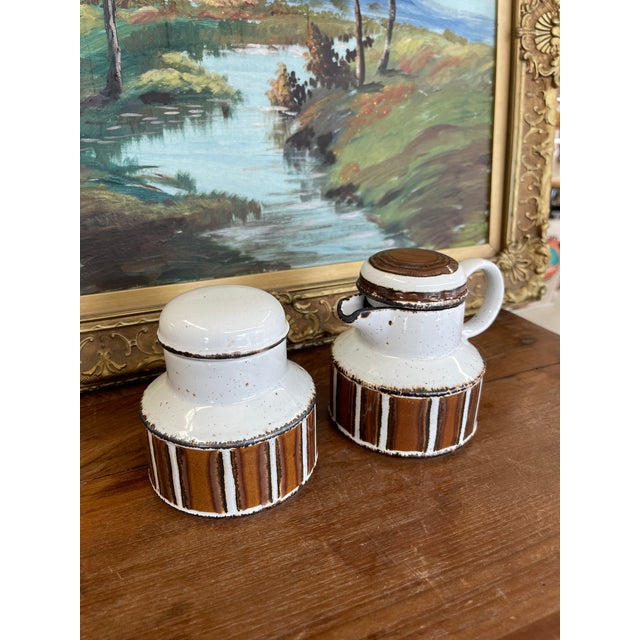 This vintage ceramic creamer and lidded sugar bowl set was produced by Midwinter Pottery in England, a leading name in...