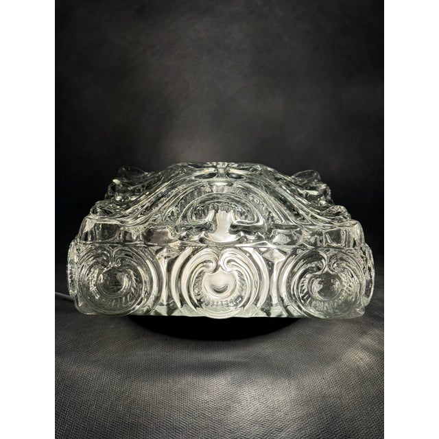 Decorative flush mount ceiling light made of thick pressed glass with an ornate relief pattern. A classic example of...