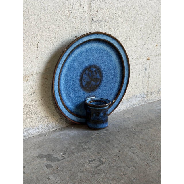 This vintage ceramic chamberstick features a circular wall plaque backing with an attached cylindrical candle cup. The...