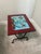 Charming French mid-century side table and magazine rack featuring a hand-decorated ceramic tile top with a colorful...