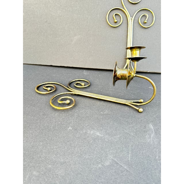 Brass candle wall sconces with an elegant, decorative design featuring scrollwork or spiral motifs at the top. They have a...