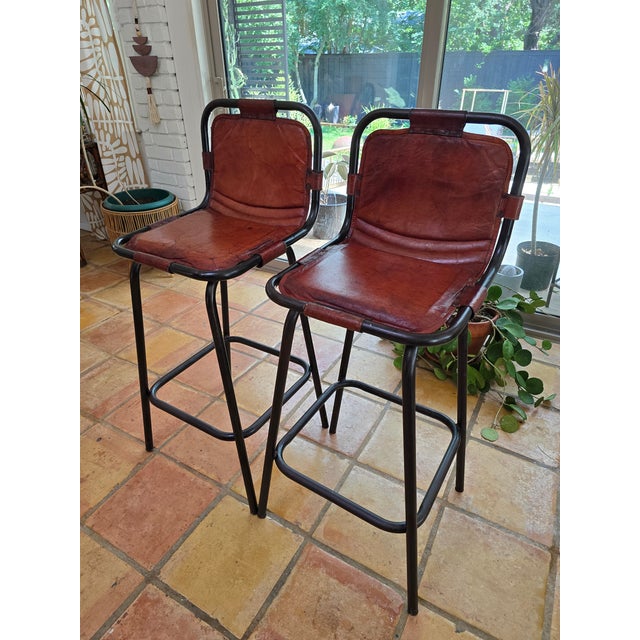Pair of barstools in the manner of French architect, Charlotte Perriand. Black enameled steel & brown leather. France, c....