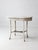 This early 20th-century white wicker table features a softly worn painted finish, an oval wood plank top, and layered...