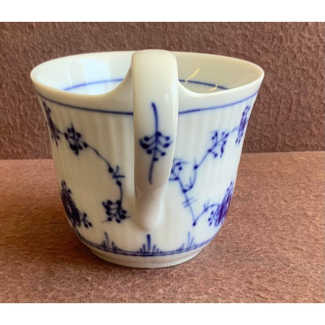 Fine white porcelain with vertical fluted texture; hand painted floral motif, a blue ring on inner rim and a high looped...