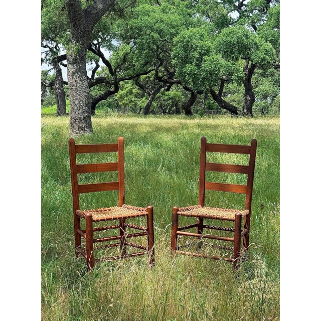A Pair of Antique Primitive Ladderback Roped Seat Folk Art, Farm Chairs, Early 1900s. The color is a rich deep...
