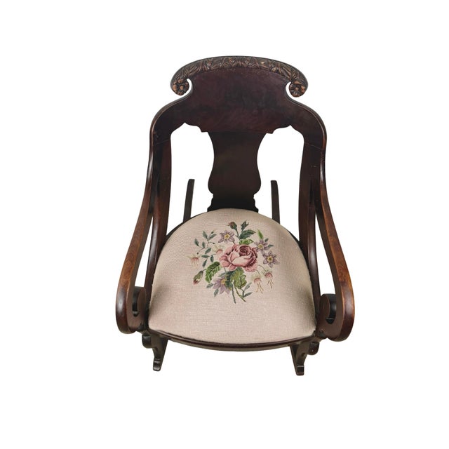 A striking antique American Classical style rocking chair featuring a sculptural carved wood frame, large scrolling arms,...