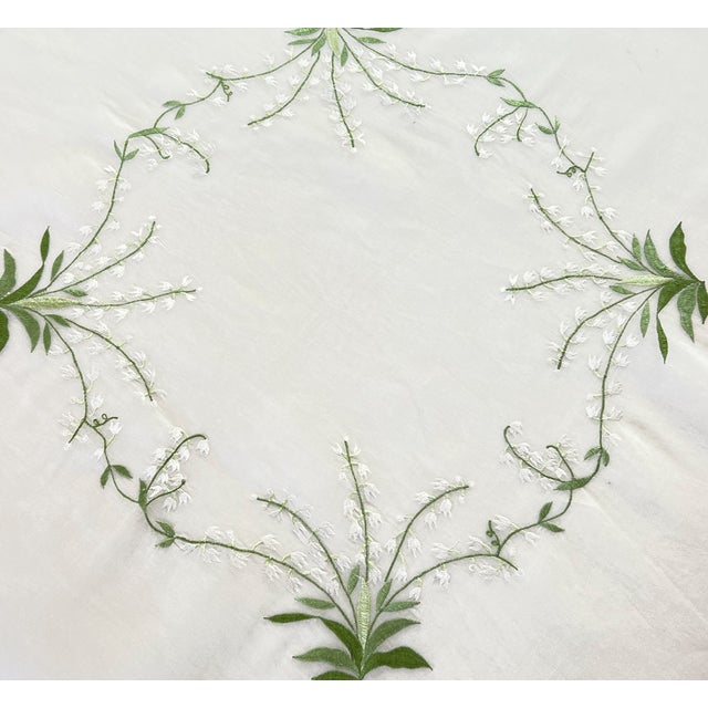 70" square white organdy tablecloth featuring four embroidered Lily of the Valleys connected by tendrils to create a...