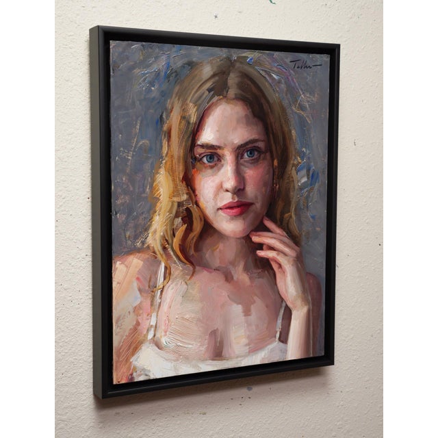 This oil on panel painting features a young woman with striking blue eyes and a contemplative expression, her hand gently...