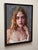 This oil on panel painting features a young woman with striking blue eyes and a contemplative expression, her hand gently...