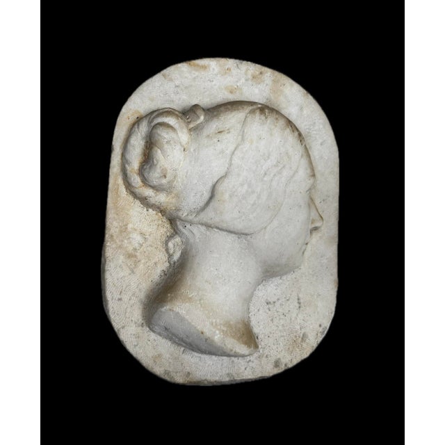 Large white marble sculpture depicting a woman's face in right profile, in a classical, neoclassical style. The modeling...