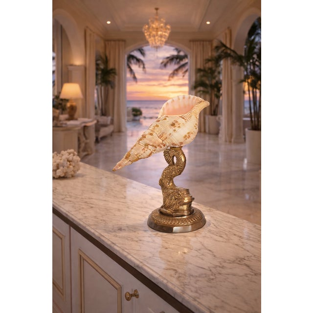 Offering a vintage Triton conch seashell placed upon a solid brass Koi fish stand, circa Mid 20th Century. This unique and...